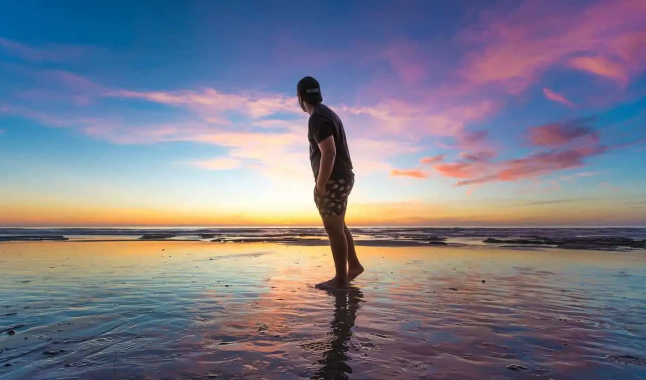 Man walking at the beach with his feet in the sand and a sunset